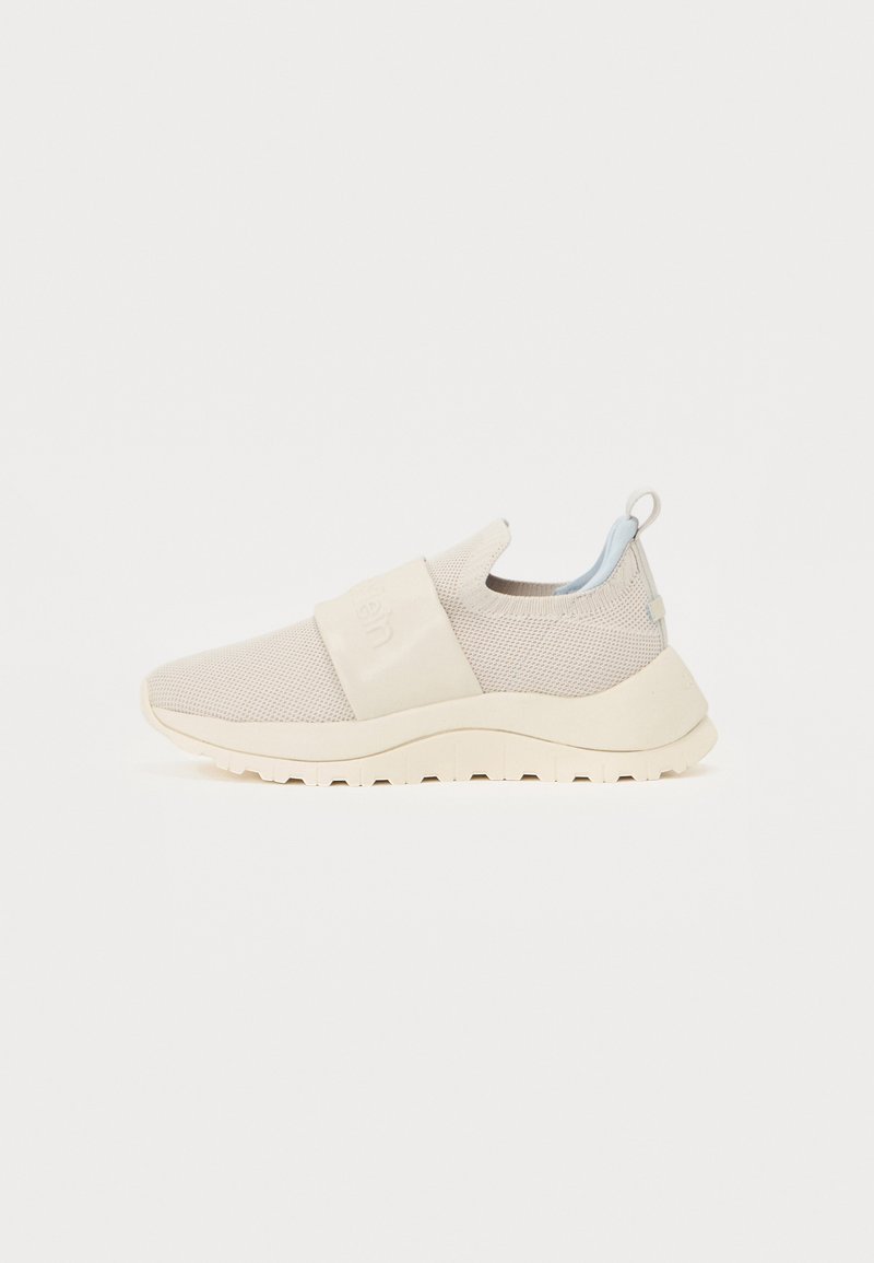 Baskets slip-on beige clair avec dessus en maille, sangle élastique et boucle au talon bleu pâle. Semelle blanche épaisse avec des crampons texturés.