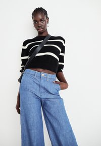 Zwart-wit gestreepte gebreide trui met een cropped ontwerp. Brede, blauwe denim jeans met zichtbare stiksels en voorzakken.