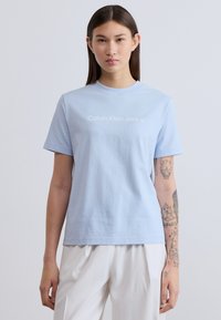 Ανοιχτό μπλε βαμβακερό T-shirt με κοντά μανίκια και στρογγυλή λαιμόκοψη. Διαθέτει το λογότυπο «Calvin Klein Jeans» σε λευκό στο μπροστινό μέρος.