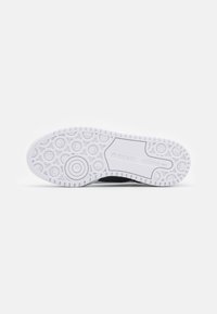Shoe sole with a textured white rubber surface featuring circular patterns and a solid central area; black upper edge visible.