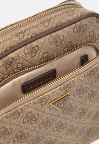 Braune Handtasche mit Muster, ausgestattet mit einem goldenen Reißverschluss, geprägtem Logo und einem dreieckigen goldenen Hardware-Akzent. Das Innenfutter hat eine satinierte Oberfläche.