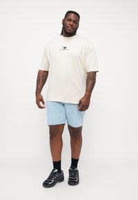 Light beige t-shirt with butterfly graphic, paired with light blue denim shorts. Black sneakers with purple accents and black socks complete the outfit.