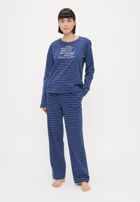 Námornícky modrý pruhovaný pyžamový set obsahuje tričko s dlhým rukávom a logom a zodpovedajúce nohavice. Mäkká tkanina s uvoľneným strihom a rovnými nohavicami.