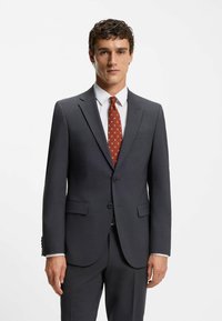 Gray suit with a tailored fit, subtle texture, and notched lapels. Paired with a white dress shirt and patterned red tie.