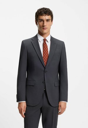 Gray suit with a tailored fit, subtle texture, and notched lapels. Paired with a white dress shirt and patterned red tie.