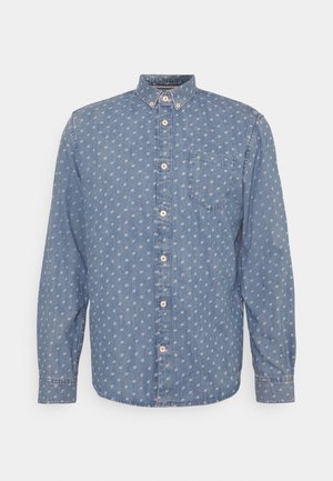 Langärmliges blaues Denim-Hemd mit Knopfleiste, weißem kleinen Punktemuster und Brusttasche vor einfarbigem Hintergrund.