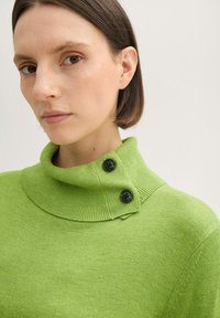 Zielony sweter dzianinowy z wysokim, prążkowanym kołnierzem. Posiada dwa czarne guziki na ramieniu. Miękka faktura, dopasowany krój.