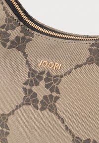 Beige taske med en struktureret overflade, der har et mørkt blomstermotiv. Guldhardware akcent med "JOOP!" logo tæt på lynlåsen.