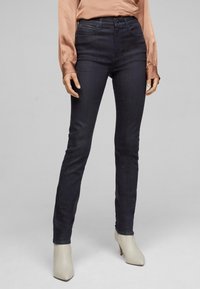 Jeans skinny de mezclilla azul oscuro con una textura suave, cintura alta y delicados detalles de costura, combinados con botas de tobillo de tacón de color claro.
