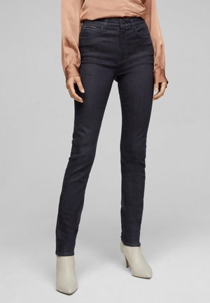 Jeans skinny en denim bleu foncé avec une texture lisse, taille haute, et détails de couture subtils, accompagnés de bottines à talons clairs.
