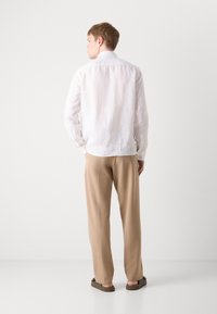 Hvit lin skjorte med lange ermer og krage, parret med beige brede bukser og mørke sandaler, sett fra baksiden.
