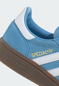 Modri semištenisice z belimi usnjenimi detajli, ki imajo teksturiran rjav gumijast podplat in zlato oznako "SPEZIAL" na strani.