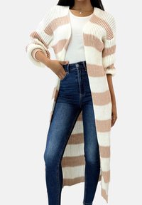 Długi kardigan wykonany z miękkiego dzianinowego materiału z naprzemiennymi białymi i różowymi paskami, z otwartym przodem i podwiniętymi rękawami. Połączony z jeansami z wysokim stanem.