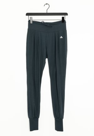 Czarne spodnie dresowe Adidas z sznurkiem w pasie i ściągaczami przy nogawkach, wiszące na czarnym wieszaku na białym tle.