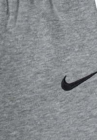 Tejido de punto gris con una textura suave que presenta un logotipo bordado de Nike en negro. Primer plano del material y detalle de la marca.