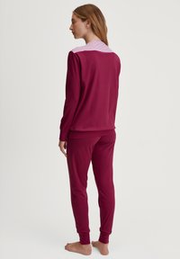 Bordeaux pyjama set met een gestreepte kraag. Lange mouwen top met geplooide schouders en bijpassende, aansluitende broek, zachte textuur.