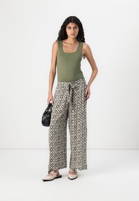 Olivengrønn tanktop, mønstrede vide bukser i jordfarger, med knyting i livet, og slip-on sko. Holder en svart veske.