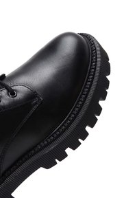 Botte en cuir noir avec bout rond, design à lacets et semelle épaisse à relief présentant des détails de texture horizontaux et verticaux.