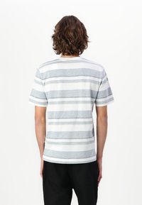 T-shirt à manches courtes rayé avec des rayures grises, blanches et subtilement jaunes. Fabriqué en tissu doux avec une coupe décontractée et un col rond.