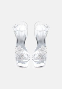 Aiškios aukštakulnės sandalės su skaidriu dizainu, ant dirželių puikuojasi trys žėrintys gėlių motyvai iš akutės akmenėlių.