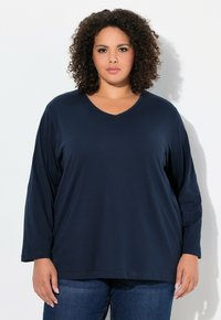 Navyblaues langärmliges V-Ausschnitt-Oberteil aus weichem Stoff, lockere Passform, mit glatter Textur und dezenten Nähten. Kombiniert mit Jeans.