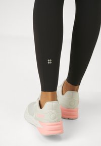 Høytlivde svarte leggings med reflekslogo på leggen, kombinert med lysegrå og rosa-acenterte joggesko med teksturert hæl.