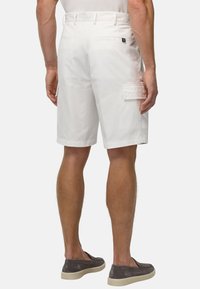 Shorts en coton blancs avec une taille ajustée, des poches arrière et une poche cargo sur le côté. Coupe slim avec une texture lisse, portés avec des chaussure à enfiler grises.