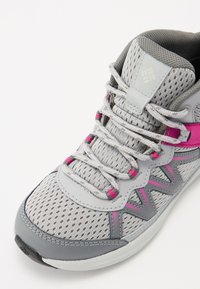 Scarpe sportive grigie con tomaia in mesh, accenti rosa e sovrapposizioni sintetiche grigie. Presentano un sistema di allacciatura e un colletto imbottito per il supporto.