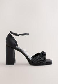 Fekete blokk sarokkal ellátott szandál, amely csomós elülső pánttal és ráncokkal, állítható bokapánttal, valamint sima szatén felülettel rendelkezik.