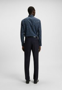 Blauw ingevoerd overhemd met een bladenpatroon, gecombineerd met op maat gemaakte donkere broeken. Het overhemd heeft een kraag en lange mouwen, met een gladde textuur.