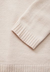 Ljusbeige stickad tröja med ribbad mudd och mjuk textur, med en slät kropp och subtila färgvariationer.