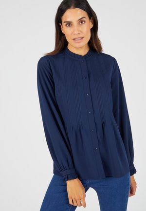 Donkerblauwe blouse met rimpel-kraag, knoopsluiting aan de voorkant, lange mouwen en verticale stikdetails. Zacht stof met een vloeiende silhout.