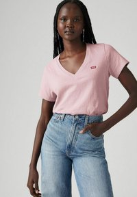 Różowa koszulka z dekoltem w serek z małym czerwonym logo Levi's, w połączeniu z jasnoniebieskimi jeansami z wysokim stanem, charakteryzującymi się klasyczną teksturą dżinsu.