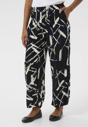 Pantalons à motifs noir, blanc et bleu, avec une coupe loose, une taille élastique et des poches latérales. Le tissu présente un aspect texturé.