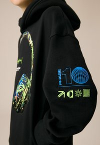 Zwarte hoodie met een kleurraf headphone-afbeelding op de voorkant en blauwe en neon groene accenten met iconen op de mouw.