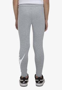Grå leggings med tettsittende passform, med en hvit logodetalj på nederste del av benet og en bred midjebånd. Kombinert med svarte joggesko.