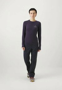 Long-sleeve purple top with a small logo and dark pants, featuring a straight cut and fabric texture suitable for active wear.