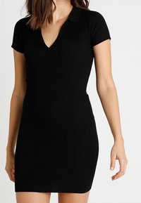 Vestito mini nero a coste con maniche corte, scollatura a V e design con colletto. Tessuto liscio e silhouette aderente.