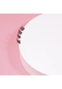 Black false eyelashes displayed on a circular white platform, against a pink background. Lashes have a wispy design and varied lengths.