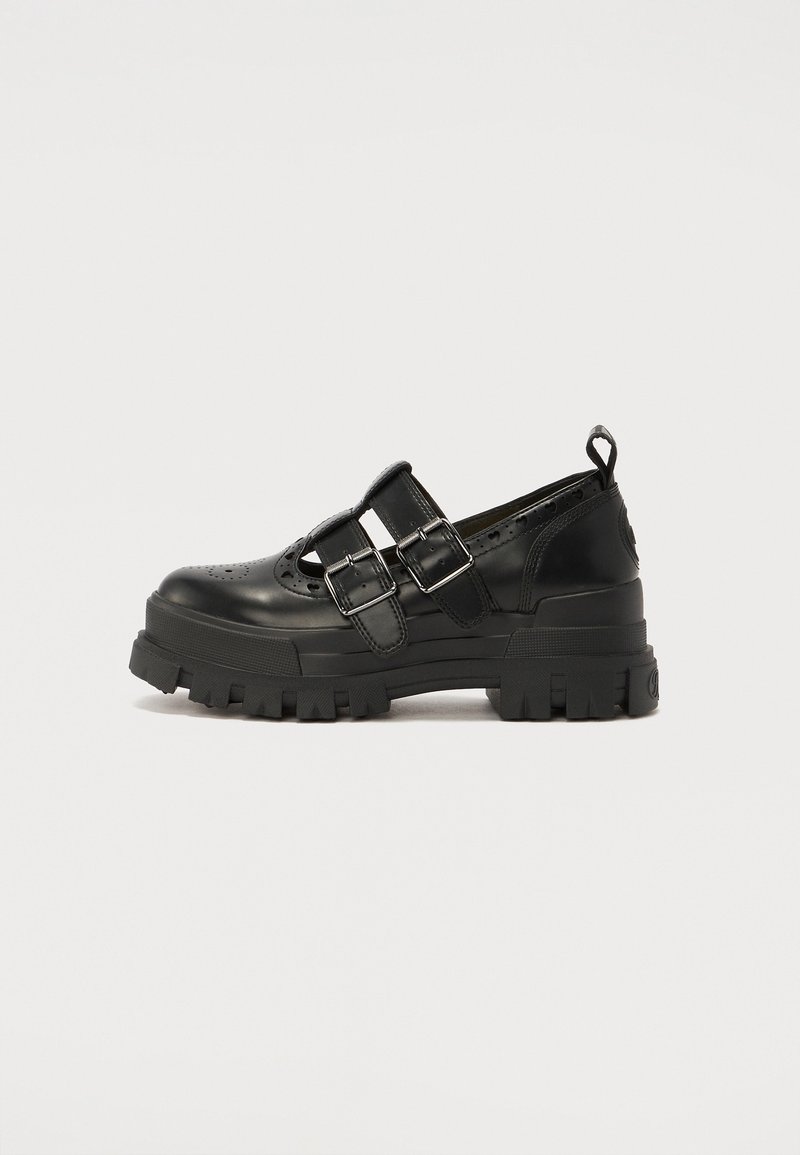 Chaussure en cuir noire avec semelle épaisse, deux brides à boucles réglables, détails perforés et languette de maintien au talon, vue de profil.