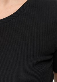 Černý úpletový top s V-výstřihem. Má krátké rukávy a strukturovanou tkaninu, která zdůrazňuje přiléhavý střih.