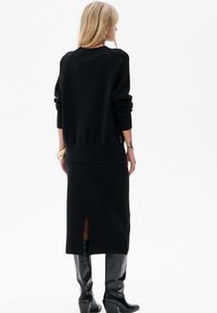 Zwart gebreid vest en midi-rok, met een achterste splits. Gecombineerd met glanzende zwarte kniehoge laarzen. Glad textuur, eenvoudig ontwerp.