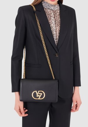 Borsa a tracolla in pelle nera con catena dorata, forma rettangolare e un accentuato logo dorato sul fronte. Materiale testurizzato.