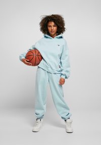 Light blue oversized hoodie with cuffed sleeves, paired with matching joggers and white high-top sneakers, holding a basketball.