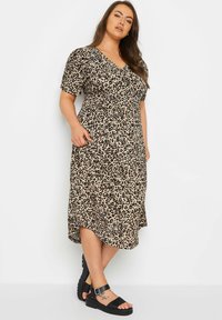 Valkoinen leopardikuvioinen kietaisumekko, jossa on lyhyet hihat, V-pääntie, vyötäröstä kireä ja sivutaskut; yhdistetty mustiin remmisandaaleihin.