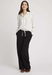 Chemisier blanc à manches longues avec des pois noirs, col et boutonné. Associé à un pantalon large noir et des mocassins bordeaux.