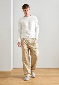 Sweat-shirt blanc, pantalon plissé beige et baskets grises ; design simple avec une texture lisse, coupe décontractée et couleurs neutres.