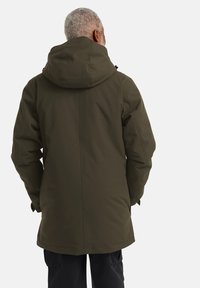 Parka olive en vert avec capuche, fabriquée à partir d'un tissu texturé. Présente une coupe droite et est plus longue avec des fermetures cachées.
