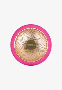 Dispositif de soin de la peau circulaire avec un extérieur en silicone rose et un intérieur métallisé doré, présentant de petits points texturés et le nom de la marque "FOREO."