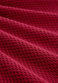 Strukturierter roter Stoff mit einem Rautenmuster, das erhabene Konturen und ein weiches Erscheinungsbild aufweist, sanft in Schichten drapiert.